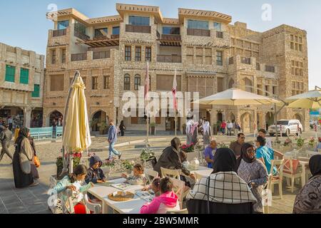 Femmes et hommes qatari à Souk Waqif, Doha Qatar marchant dans la rue et assis dans un restaurant à la lumière du jour Banque D'Images