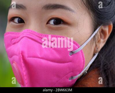 La jeune femme vietnamienne porte un masque rose avec boucle d'oreille et valve respiratoire pendant la pandémie de 2019/20 du virus corona. Banque D'Images