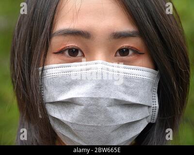 Une jeune femme vietnamienne aux yeux magnifiques porte un masque facial jetable chirurgical pendant la pandémie de 2019/20 du virus corona. Banque D'Images