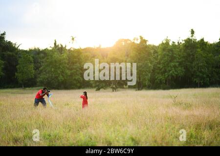 père prend une photo de sa fille dans le jardin, champ, soirée, coucher de soleil, temps de famille, sensation chaude Banque D'Images