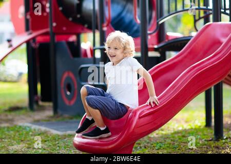 Enfant jouant sur l'aire de jeux extérieure. Les enfants jouent sur l'école ou l'école maternelle cour. Kid active sur diapositive colorées et swing. Activité d'été sain pour chi Banque D'Images