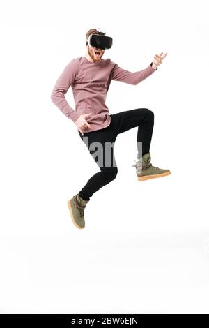 Jeune homme en lunettes de réalité virtuelle sautant et jouant comme une guitare sur fond blanc. Portrait d'un garçon joyeux portant des lunettes de réalité visuelle Banque D'Images