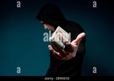 Un homme tient de l'argent et cache son visage. Silhouette sombre avec une seringue Banque D'Images