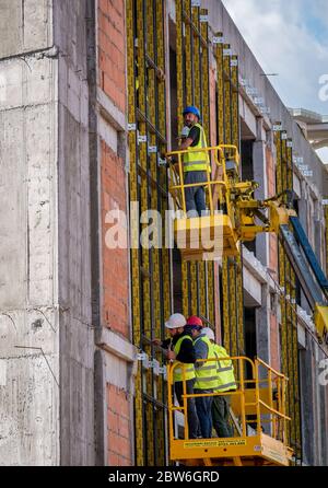 Bucarest/Roumanie - 05.16.2020: Ouvriers de la construction sur un échafaudage. Hommes travaillant dans un bâtiment à partir d'une plate-forme de table élévatrice hydraulique Banque D'Images