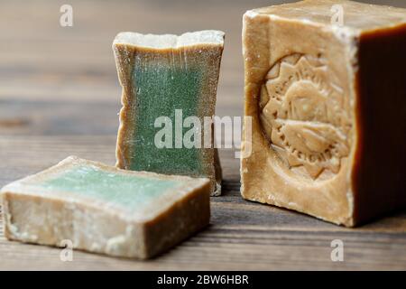 Bar et deux tranches de savon de Laurier biologique traditionnel alep sur fond de bois brun. Concept de traitement de la peau Banque D'Images