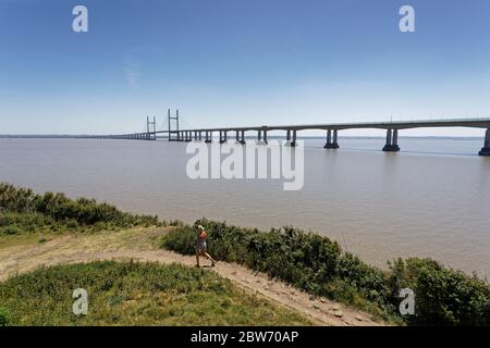 Une femme marche le long du chemin qui longe l'estuaire de la rivière Severn qui surplombe le pont du Prince de Galles Banque D'Images