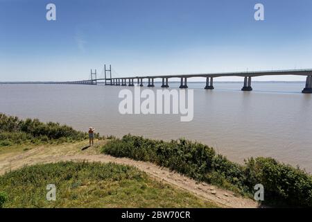 Une femme marche le long du chemin qui longe l'estuaire de la rivière Severn qui surplombe le pont du Prince de Galles Banque D'Images