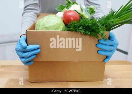 Le volontaire en gants tient des légumes de boîte de don de nourriture pour aider les pauvres. Donner la boîte avec les aliments Banque D'Images