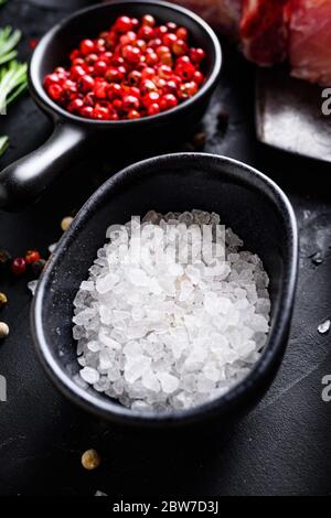 Sel de mer dans un bol noir et herbes de romarin gros plan sur la table en pierre noire avec des épices et de la viande crue près de la vue latérale sélective foyer vertical. Banque D'Images