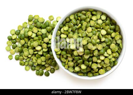 Pois verts séchés dans un bol en céramique blanc à côté d'une pile de pois coupés isolés sur du blanc. Vue de dessus. Banque D'Images