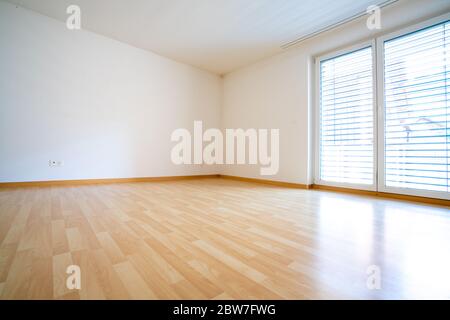 Une vue sur une chambre très lumineuse et lumineuse avec parquet et murs en plâtre blanc et une grande fenêtre avec stores Banque D'Images