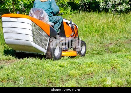 Un parc bien entretenu avec une pelouse taillée grâce à un jardinier travaillant avec une tondeuse à gazon professionnelle par temps ensoleillé. Banque D'Images