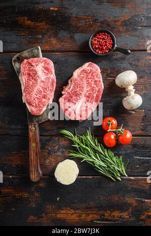 Bio Top Blade steak, viande crue, boucherie de bœuf marbré coupé sur le couteau de boucher métallique avec du romarin et des herbes de ferme sur fond de table en bois ancien Banque D'Images