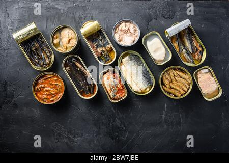 Boîte de Saury, maquereau, crats, sardines, pilchard, calmar, thon ouvert et fermé sur fond d'ardoise noire espace de vue du haut pour le texte en bas. Banque D'Images