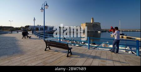 VILLANOVA, APULIA, ITALIE - 28 MARS 2018: Les gens se reposent dans le petit port avec le château médiéval sur le bord de mer à Villanova, Puglia, Italie Banque D'Images