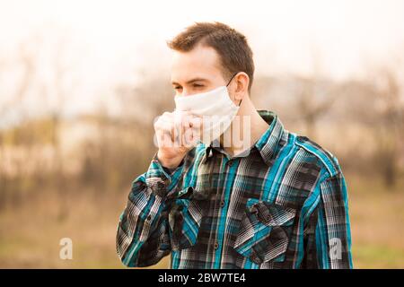 Grippe, froid concept. Portrait d'un jeune homme malade, toux, portant un masque facial à l'extérieur Banque D'Images