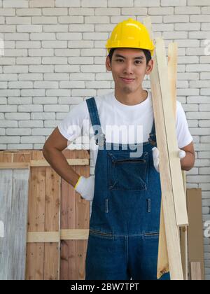 Un charpentier asiatique portant un casque jaune, portant du bois pour la fabrication de meubles dans la salle d'atelier. Banque D'Images