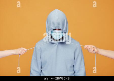Mains humaines étirant des cordons de sweat à capuche bleu portés par un jeune homme dans un masque de protection debout devant l'appareil photo en isolement Banque D'Images