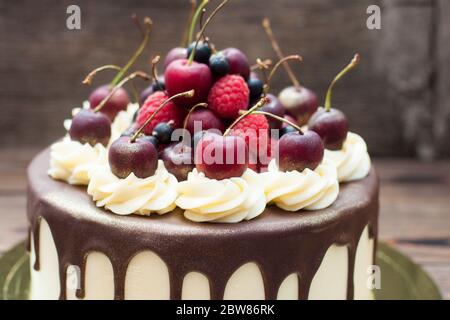 Gâteau d'anniversaire décoré de chocolat fondu, de crème fouettée et de cerises fraîches. Arrière-plan rustique. Banque D'Images