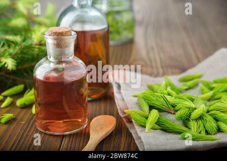 Bouteilles de potion, sirop ou miel de bourgeons et aiguilles de sapin, brindilles de sapin sur table en bois. Banque D'Images