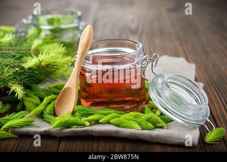 Pot de confiture, sirop ou miel de bourgeons et aiguilles de sapin, brindilles de sapin sur table en bois. Faire des pointes d'épicéa bourrage à la maison. Banque D'Images