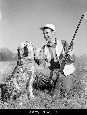DANS LES ANNÉES 1960, HOMME SOURIANT CAILLE HUNTER AGENOUILLÉ AVEC POMPE À POMPE À FUSIL DE CHASSE PRENDRE L'OISEAU DE LA BOUCHE DE SON CHIEN DE RETRIEVER ANGLAIS - G5149 HAR001 HARS MÂLES HUNTER ANGLAIS B&W CHASSE À GENOUX COMPÉTENCE ACTIVITÉ AMUSEMENT BONHEUR MAMMIFÈRES AVENTURE SON HOBBY LOISIR CANINES HOBBIES SAVOIR PASSE-TEMPS DISPOSITIF DE RÉGLAGE AUTOMNE PLAISIR ANGLAIS SETTER CONNEXION RETRIEVER WILD JEU CANINE COOPÉRATION ARME À FEU CHASSEURS MAMMIFÈRES ADULTE MOYEN-ADULTE HOMME DÉTENTE TOGETHERNESS AMATEUR AUTUMNAL OISEAU CHIEN NOIR ET BLANC CAUCASIEN PLAISIR ETHNIQUE CHUTE FEUILLAGE HAR001 OLD FASHIONED Banque D'Images