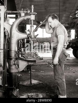 ANNÉES 1950 HOMME MACHINISTE DEBOUT TRAVAILLANT UNE PERCEUSE PRESSE FOREUSE FORAGE D'UN TROU DANS UN COLLIER EN MÉTAL OPÉRATEUR DE MACHINE LOURDE - I3271 HAR001 HARS COMPÉTENCES MÉTIER OPÉRATEUR OPÉRATEUR MANUEL DE MACHINES DE FORAGE CARRIÈRES TRAVAIL A DANS LES PROFESSIONS CONNEXION MANUEL TRAVAIL EMPLOYÉ COMMERCE BLEU JEANS JEUNE ADULTE HOMME NOIR ET BLANC ORIGINE ETHNIQUE CAUCASIENNE HAR001 MACHINISTE ANCIEN MODE Banque D'Images