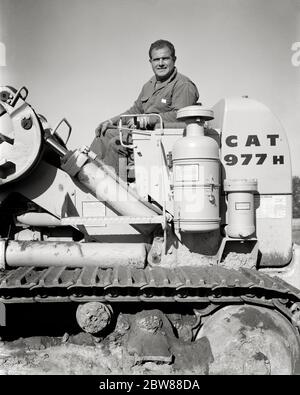 ANNÉES 1960 HOMME SOURIANT CONDUCTEUR D'ÉQUIPEMENT DE CONSTRUCTION REGARDANT LA CAMÉRA ASSIS SUR LA CONDUITE CATERPILLAR TERRASSEMENT BULDOZER - I4866 HAR001 HARS B&W HOMME D'ÂGE MOYEN CONTACT ŒIL BLEU COLLIER COMPÉTENCE MÉTIER PROFESSIONNEL CONDUCTEUR MANUEL FORCE BULLDOZER BAS ANGLE PUISSANT INDÉPENDANT FIERTÉ DU TRAVAIL SUR L'AUTORITÉ EMPLOIS CONCEPTUEL SÉPARÉ SOLITAIRE SEUL EMPLOYÉ SOLO COMMERCE CATERPILLAR ADULTE MOYEN ADULTE HOMME MOYEN-ADULTE NOIR ET BLANC RACE BLANCHE HAR001 TRAVAIL INDIVIDUEL ANCIEN MODE Banque D'Images