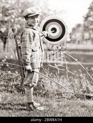 1920 ANNÉES 1930 GARÇON SOURIANT ARCHER REGARDANT L'APPAREIL PHOTO PORTANT TANGA LAINE CASQUETTE CHANDAIL TIRANT FLÈCHE DE CIBLE TAUREAUX OEIL - Q37537 CPC001 HARS FIER RURAL ATHLÉTISME NATURE COPIE ESPACE PLEIN-LONG TIR À L'ARC INSPIRATION PRATIQUE HOMMES RISQUE FLÈCHE ATHLÉTIQUE CONFIANCE B&W OEIL CONTACT OBJECTIFS BONHEUR GAI AVENTURE LOISIR ET EXCITATION RÉCRÉATION ACCOMPLISSEMENT ARCHER AUTOMNE FIERTÉ SOURIT ARC ET FLÈCHE CONNEXION ATHLÈTES JOYEUSE STYLE WOOLEN ANONYME BULL'S GROWTH JUVÉNILES AUTOMNAL TAUREAUX NOIR ET BLANC RACE BLANCHE AUTOMNE FEUILLAGE ANCIEN MODE Banque D'Images