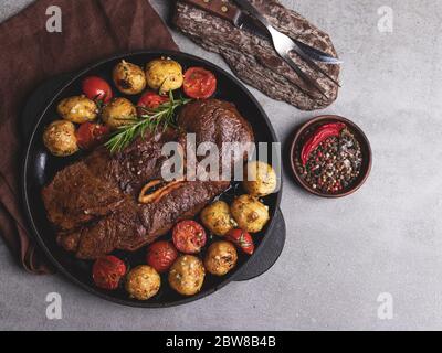 steak de bœuf grillé avec os, pommes de terre nouvelles grillées tomate avec ail dans une casserole Banque D'Images