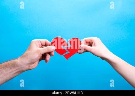 Mains de l'homme et de la femme déchirant un coeur en papier rouge sur fond bleu Banque D'Images