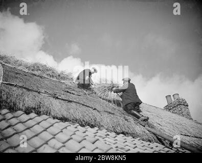 Les hommes travaillent sur un toit en tuiles en mettant du chaume sur le toit d'un chalet à Orpington . 1935 . Banque D'Images