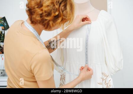 Dans un studio, la couturière prend des mesures à partir d'une robe sur un mannequin Banque D'Images
