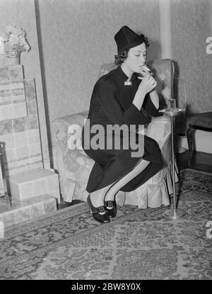 Miss Muriel Oxford est assis près du feu ayant une cigarette . Banque D'Images