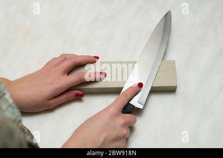 couteau, pierre à affûter et mains de femme. Femme et travail masculin Banque D'Images