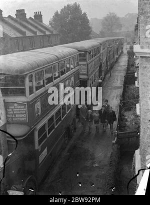Un groupe d'enfants qui passent devant un seririers de London transport bus qui sont garés dans une rue latérale à Sidcup , Kent . 1939 Banque D'Images