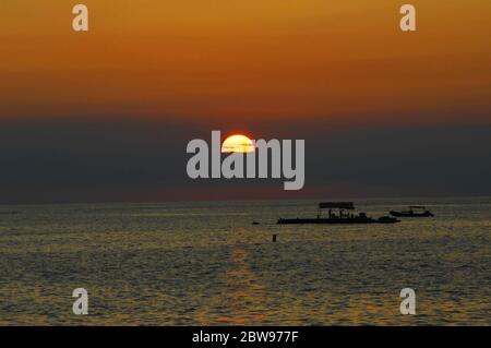 Big Island coucher de soleil silhouettes bateau à fond plat et skiff. Le soleil est une boule de feu et teinte le ciel une orange vif. Banque D'Images