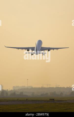 Avion de tourisme à large carrosserie qui se dévolte au coucher du soleil au-dessus de la piste, vue arrière, espace de copie. Avion voler vers le haut, ciel jaune sur fond. Vacances, aviation Banque D'Images