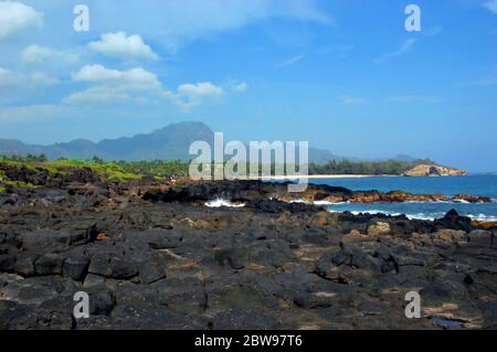 Paysage immense et petit homme. Tourist se trouve sur les rochers de lave du rivage de Shipwreck Beach. Les montagnes Haupu sont dans l'arrière-plan avec un ciel bleu et de la bl Banque D'Images