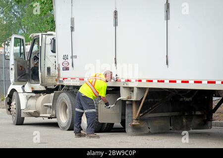 Un conducteur de camion portant un gilet de sécurité et des gants de travail effectue des réglages sur un camion semi-remorque blanc. Photo. Banque D'Images