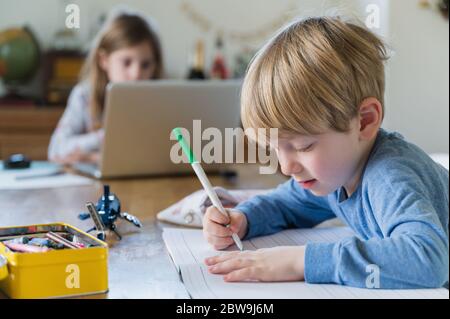 Garçon (4-5) et fille (6-7) faisant leurs devoirs à table Banque D'Images