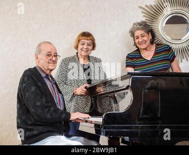 Femmes âgées écoutant un homme jouant du piano Banque D'Images