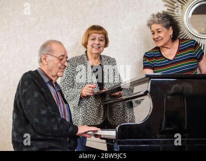 Femmes âgées écoutant un homme jouant du piano Banque D'Images