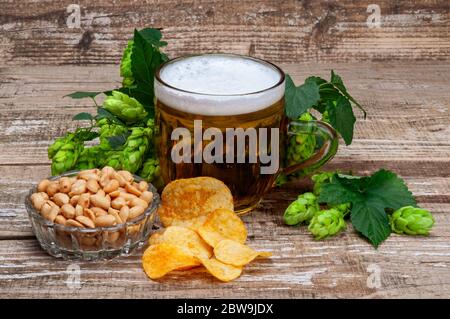 Un verre de bière avec des houblon vert, des arachides et des chips. Banque D'Images