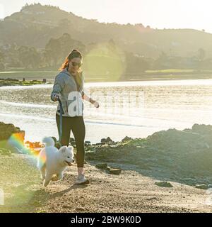 États-Unis, Californie, San Francisco, femme avec un chiot de Samoyed en train de courir sur la plage Banque D'Images