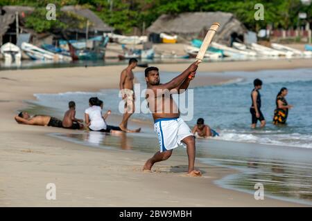 Un homme aime frapper une balle tout en jouant au cricket sur la plage de sable de la baie d'Arugam, sur la côte est du Sri Lanka. Banque D'Images