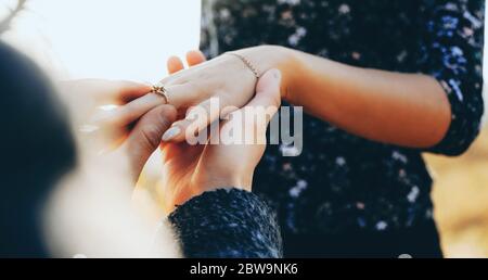 Homme caucasien à genoux demandant le mariage de sa petite amie tout en mettant sur son doigt l'anneau de mariage Banque D'Images
