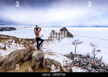 Lac Baikal, Russie - 13 mars 2020 : l'homme se dresse au bord d'un rocher et pratique du yoga près du cap Burhan sur Shamanka Rock dans l'île d'Olkhon Banque D'Images