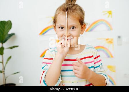 Portrait de la jeune fille heureuse d'âge préscolaire avec brosse devant des peintures arc-en-ciel Banque D'Images