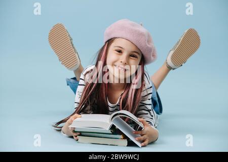 Bonne petite fille souriante dans un béret français couché sur le sol avec le livre Banque D'Images